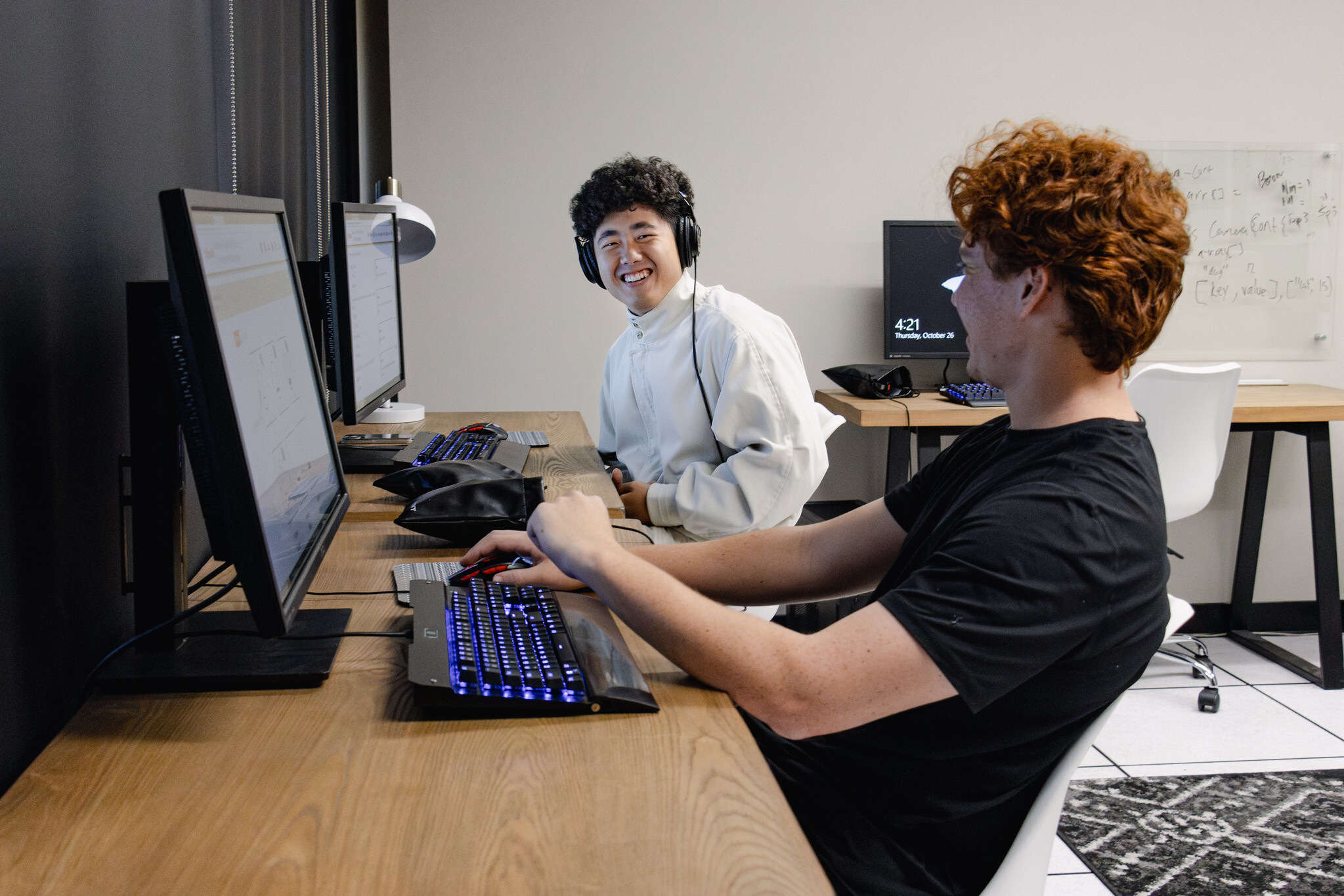 Two students smiling in front of computers.