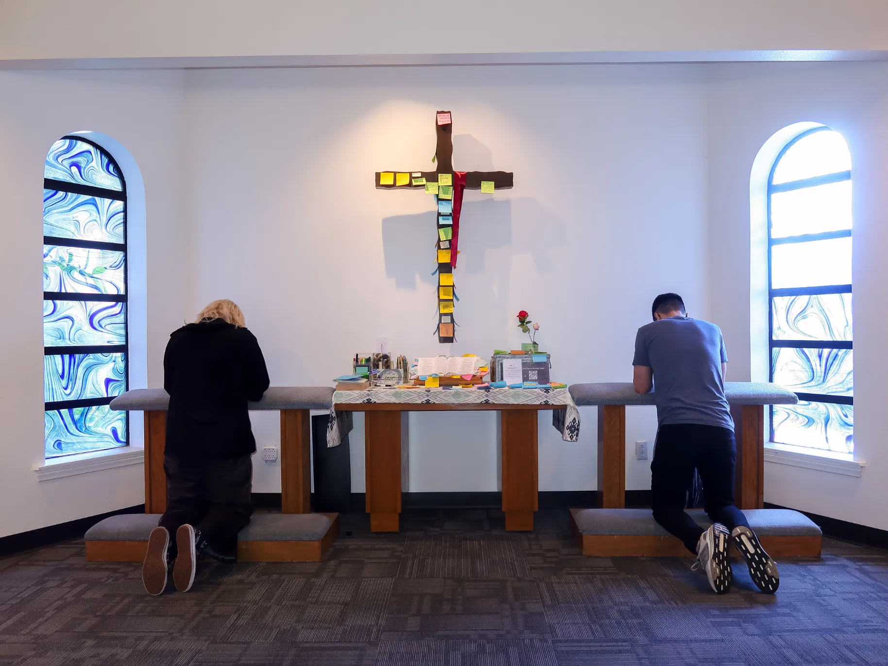 Two students kneel and pray before a cross.