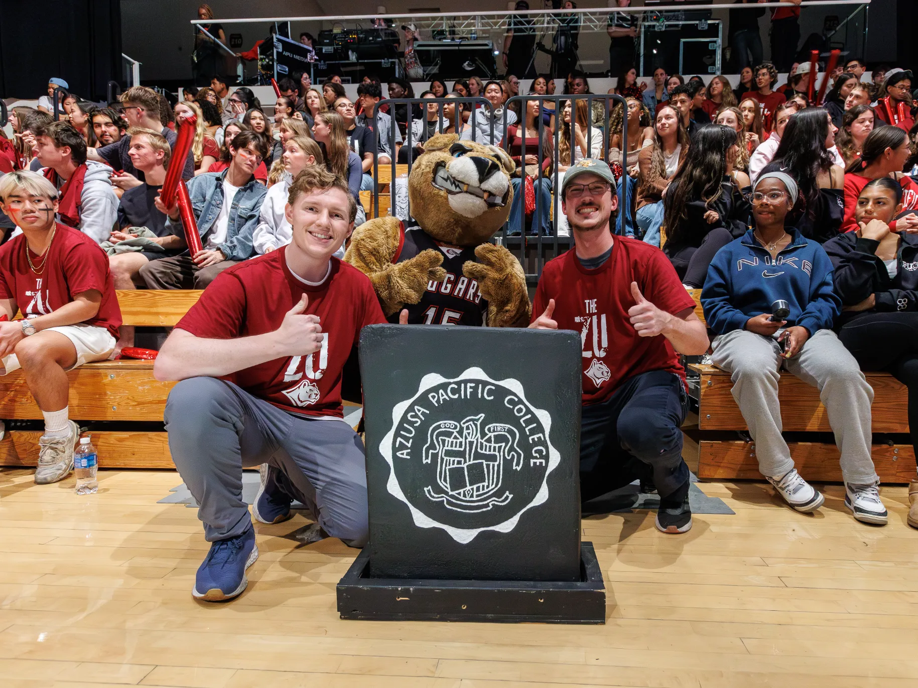 Two APU students and the cougar mascot pose with the rock