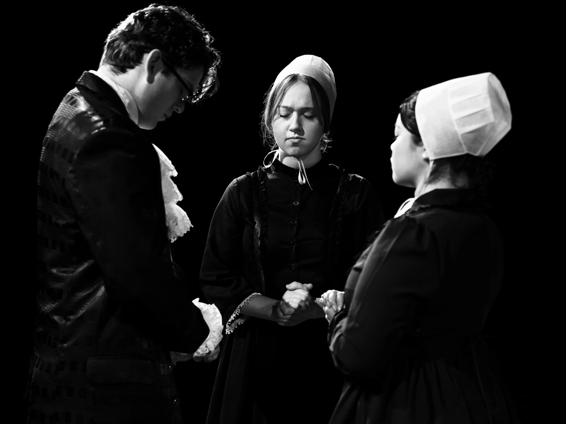 A group of actors pray together on stage